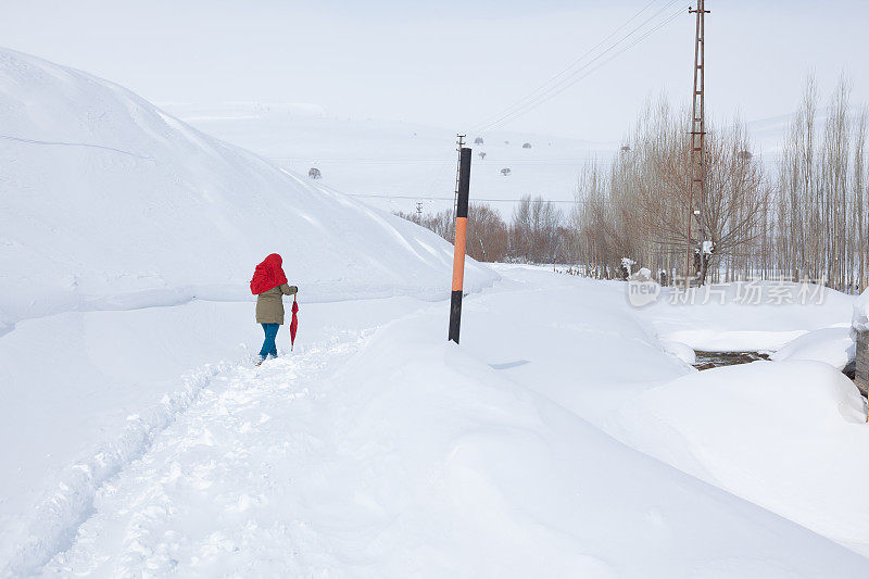 成年妇女穿着暖和的衣服在雪地上行走在农村