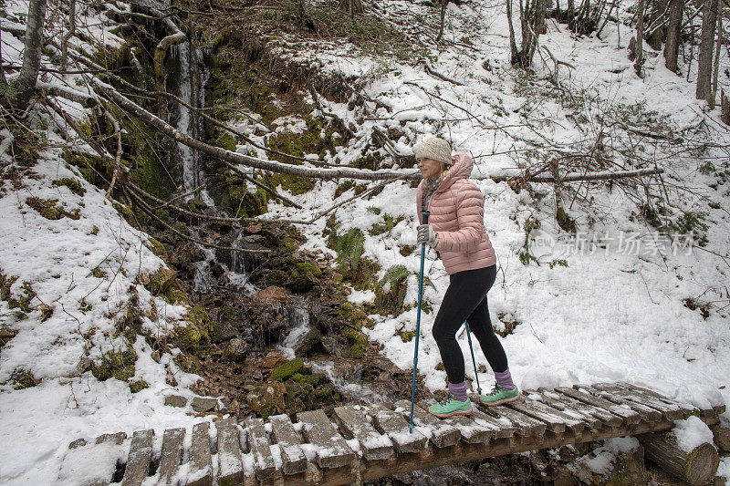 女性徒步旅行者走过被雪覆盖的木板路