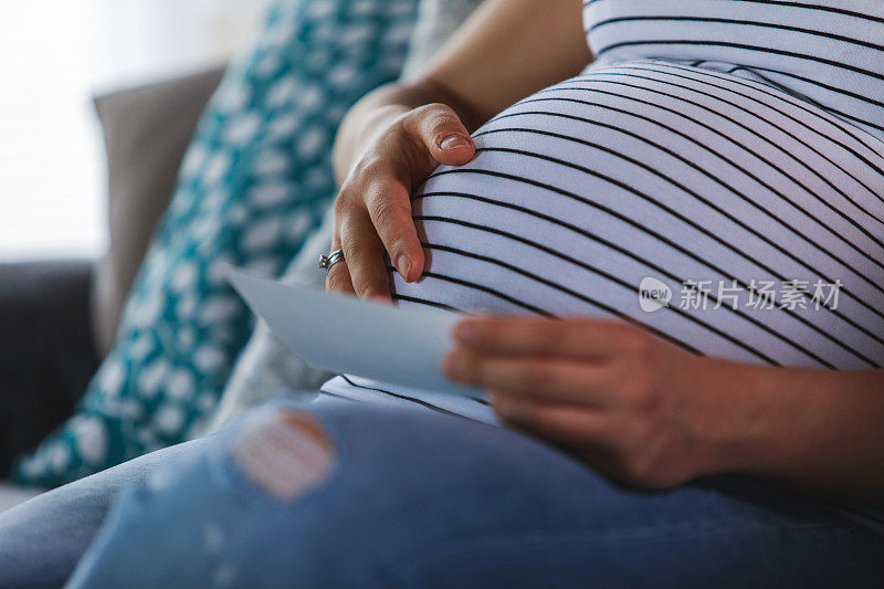 近距离的孕妇抱着她的肚子，而看她的宝宝的超声波图像