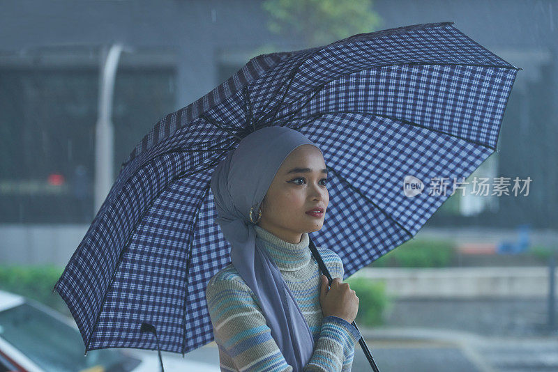 美丽年轻的亚洲穆斯林在雨天使用伞