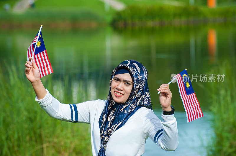 两名马来西亚妇女戴着头巾挥舞着马来西亚国旗庆祝默迪卡独立日