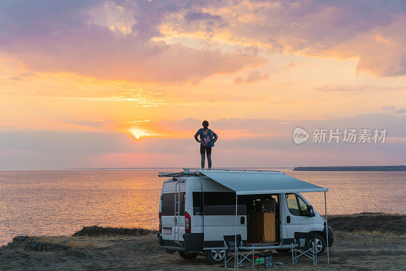 日落时分，一个女人在海边露营车的屋顶上跳舞