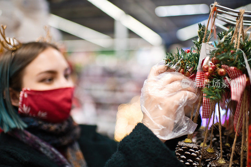 2019冠状病毒病期间，年轻女性戴着防护口罩和手套在圣诞购物