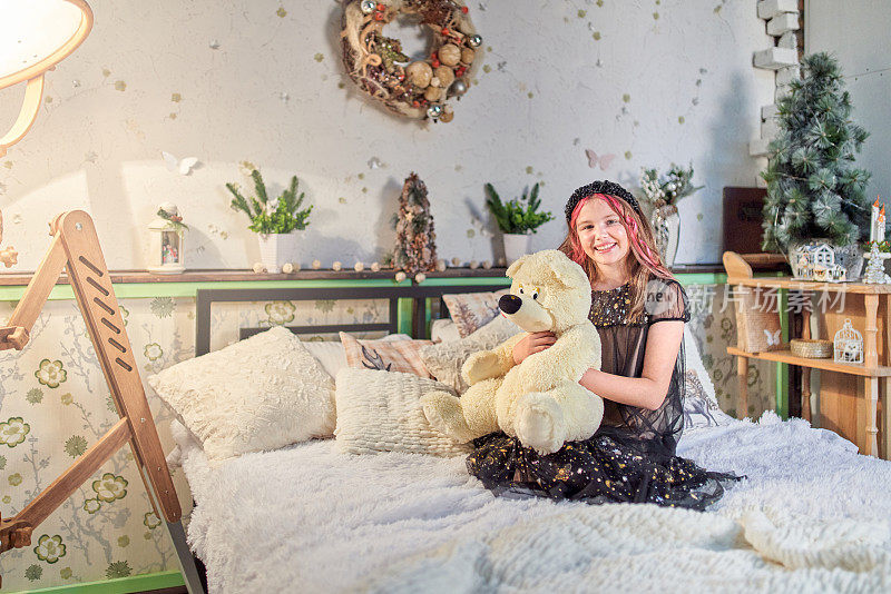 笑容可人的女孩抱着白色泰迪熊坐在圣诞装饰的卧室里