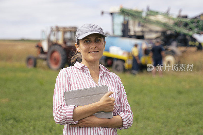 一个年轻的农妇在田地里工作的肖像，在喷洒庄稼的时候操作一个现代的作物喷雾器。在一个阳光明媚的日子里，有机农场的收获季节。农作物喷雾器使用远程控制。