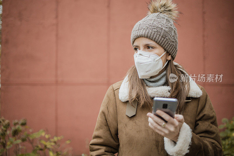 一名妇女戴着口罩在街上使用手机