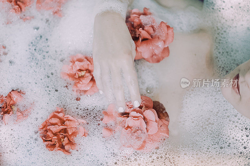 泡在泡泡和粉红玫瑰浴中的女性