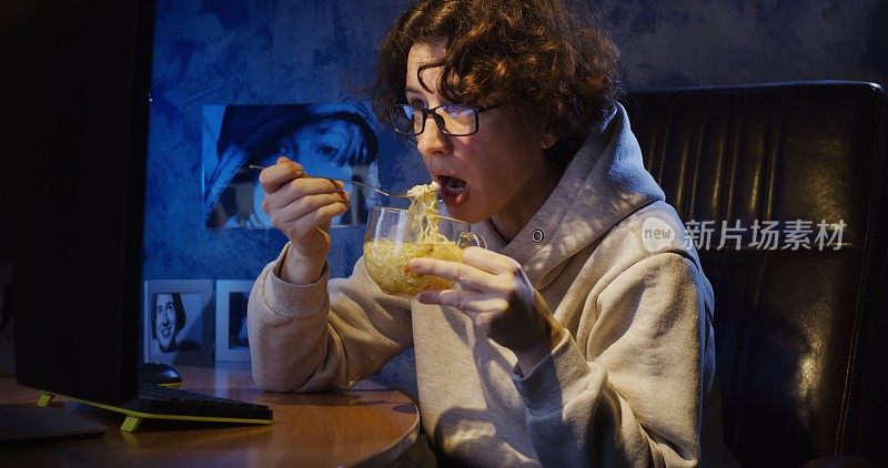 一个女人在暗室里一边吃方便面一边在电脑前看视频