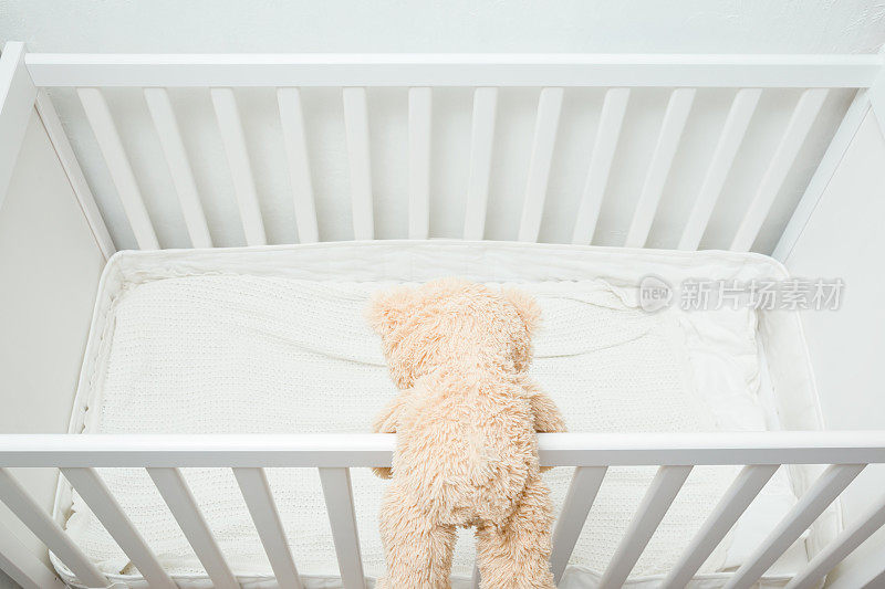 白色婴儿床栏杆上的棕色泰迪熊。婴儿安全爬床的概念。后视图。自顶向下的观点。