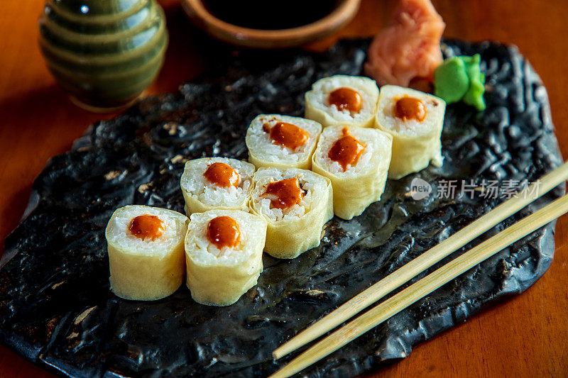 特写寿司卷与生姜和芥末在一个盘子上，商店的棍子在一边，放置在餐厅的桌子上
