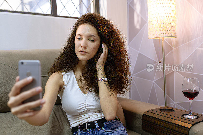 z一代的卷发女人坐在沙发上用手机拍照