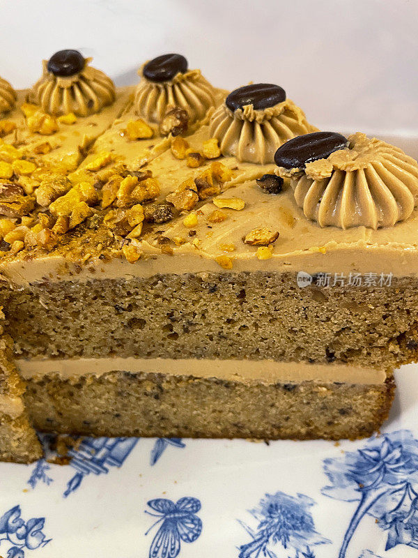 蓝色花卉图案的盘子展示切好的咖啡蛋糕，美味的甜点，覆盖着奶油，切碎的核桃和咖啡豆，高视野