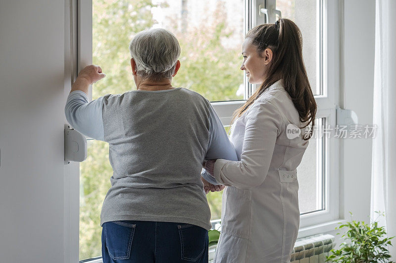 医护人员帮助站在窗户附近的老年妇女