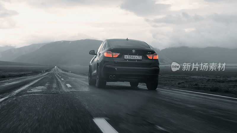黑色宝马X4在高速公路上行驶，山间风光尽收眼底。后视图