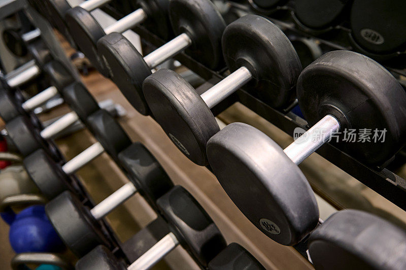 俯视图的黑色哑铃机架在体育健身中心的背景。钢哑铃。健身训练，健美和健身馆的概念。运动器材和工具主题