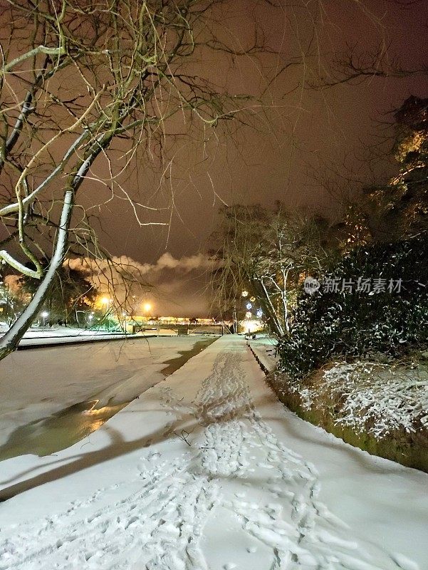 路灯和背光照明，冬雪覆盖的公园在傍晚的暮色。