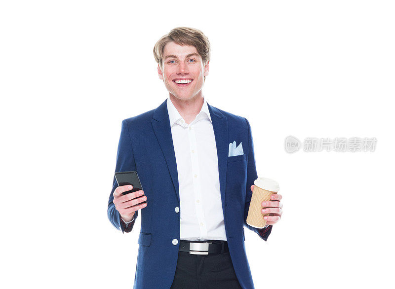 白种男性站在白色背景前，穿着夹克，拿着咖啡杯，使用智能手机