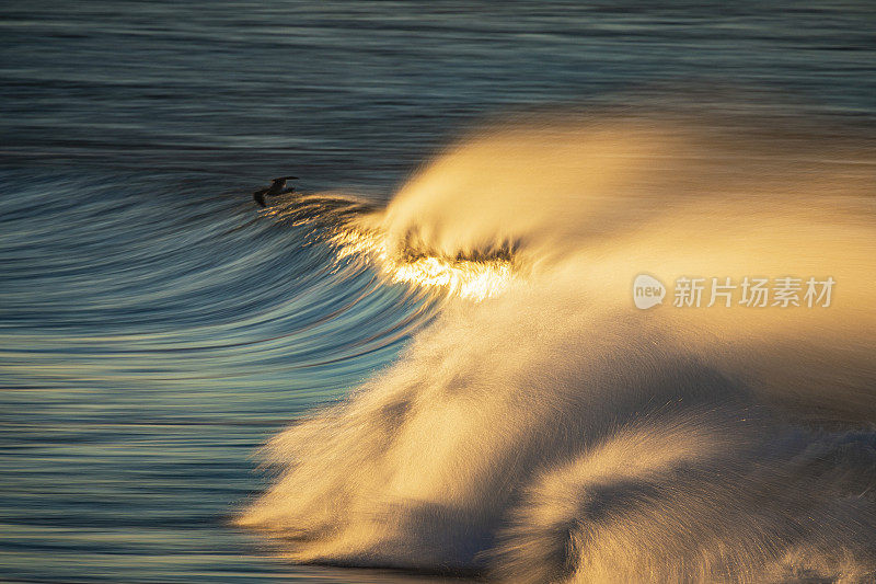 金色的海浪和强风的浪花在沙滩上反射出明亮的金色日出