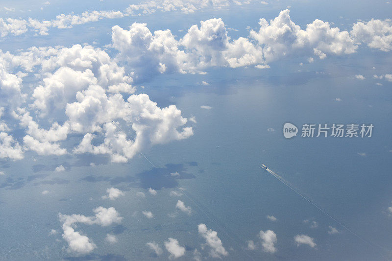 从高空的飞机窗口望去，美丽的白云漂浮在空中，碧水的海面上，阳光明媚的日子里，一条小船在水面上行驶。