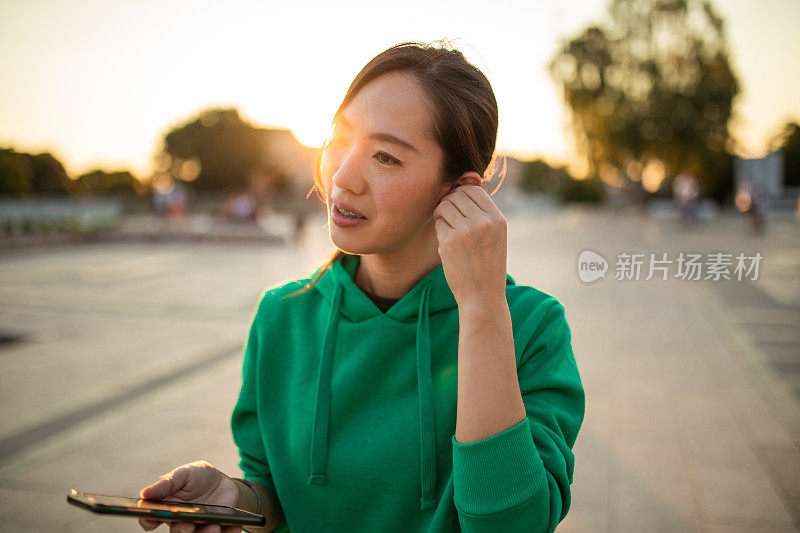 一名日本妇女在城市里使用智能手机和无线耳机