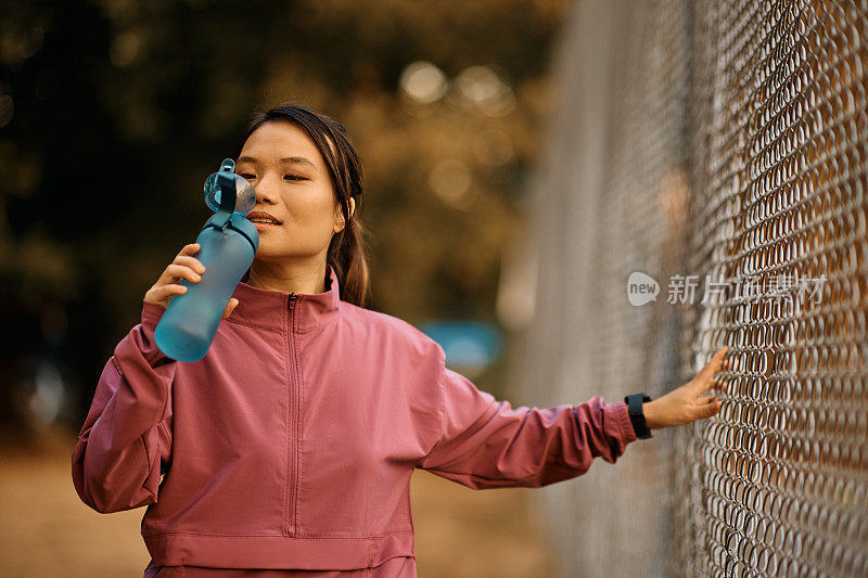 年轻的亚洲运动员在户外运动训练中休息时喝水。