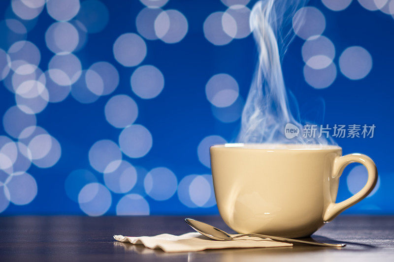 蒸汽从一大杯咖啡或茶中升起，背景是蓝色的散景