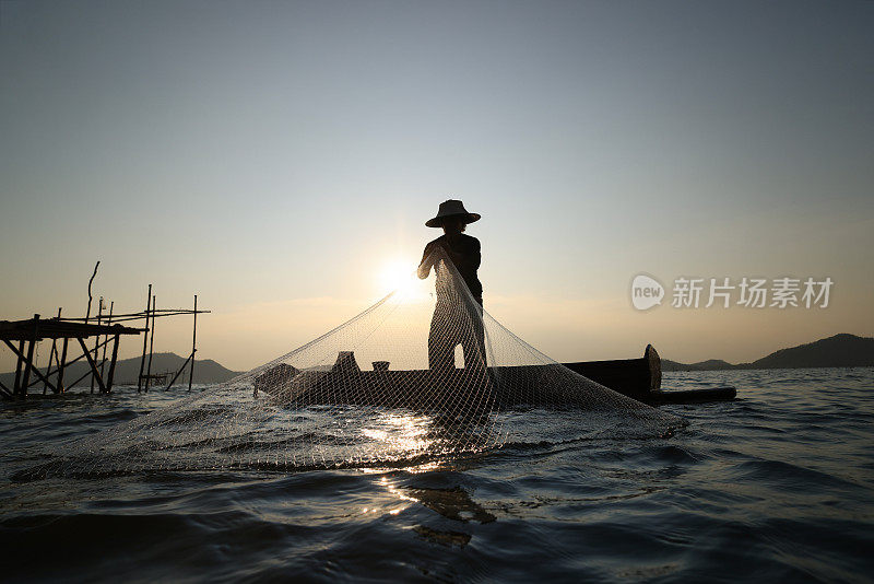 渔民在船上撒网捕鱼的生活方式，剪影渔民撒网从水库捕鱼