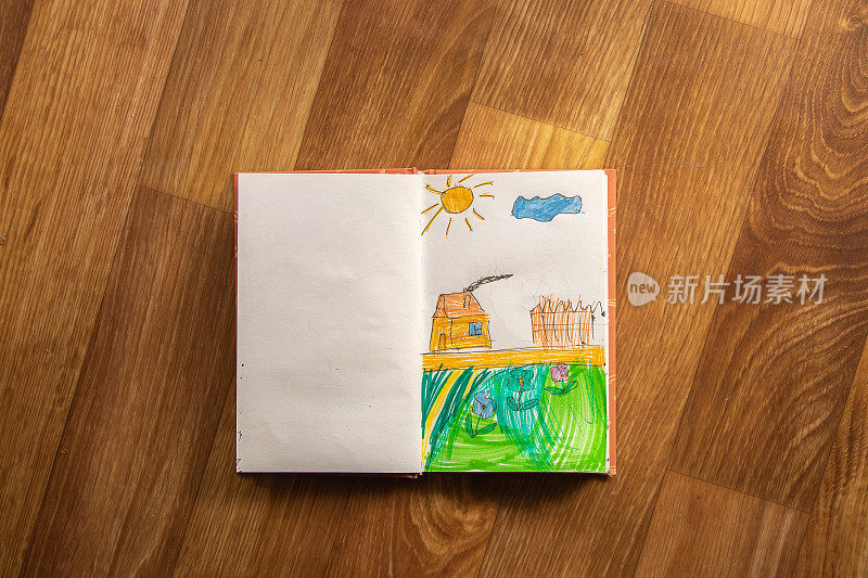 孩子在笔记本上画了一个阳光下的花房子，孩子画了一个孩子的梦想家