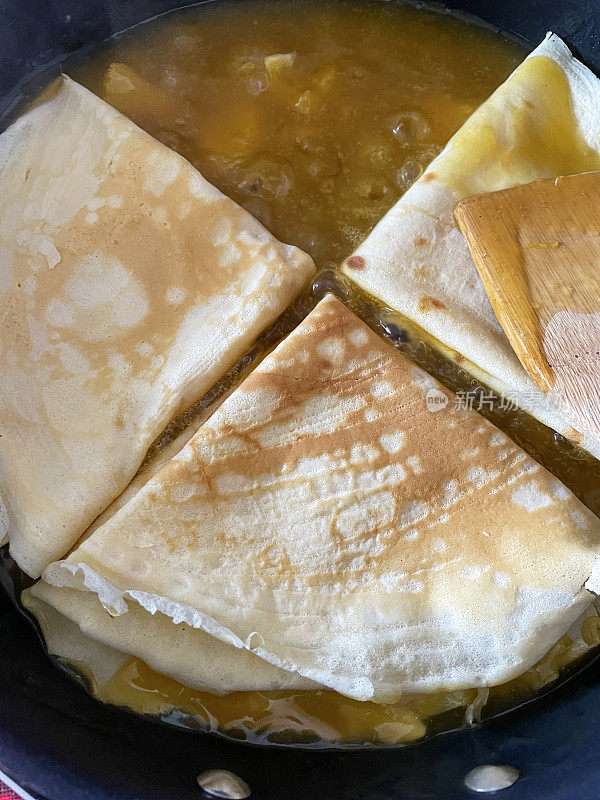 全帧图像不粘锅包含四个自制的，煮熟的法国薄饼折叠成三角形在橘子和焦糖糖浆烹饪，抬高视图
