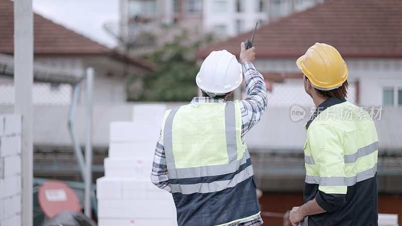 后面的观点。专业土木工程师或建筑建筑师在房屋工程施工现场与工头讨论图纸中的房屋模型。在房地产业务中穿着安全制服的承包商团队。房地产业务。