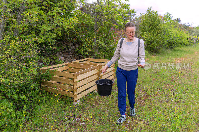 老年妇女将废物放入可回收的堆肥箱。