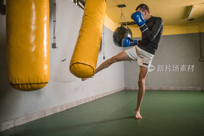 一个年轻的自由搏击运动员在健身房击打一个沙袋，锻炼他的肌肉