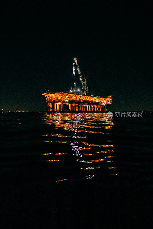 太平洋夜间的低角度照明石油钻井平台，灯光在水中的反射