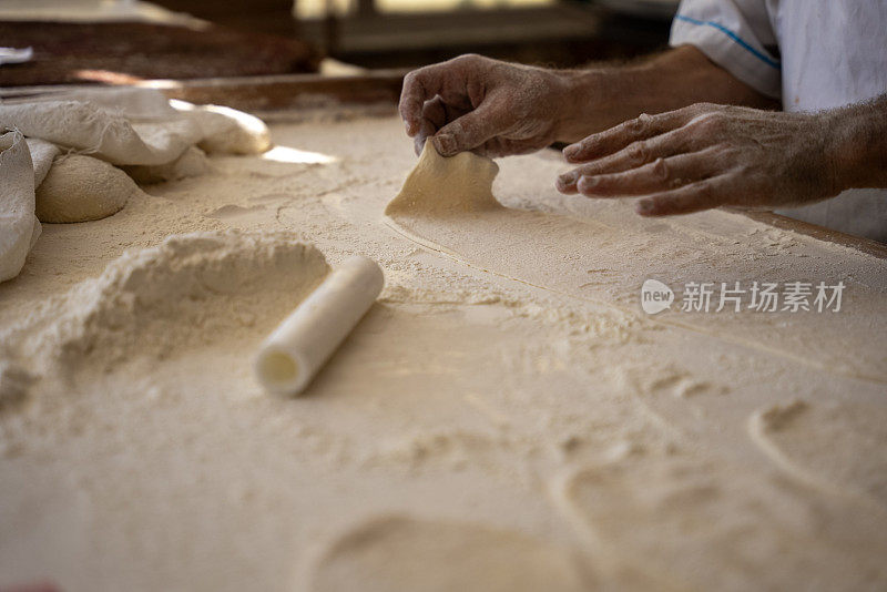 一个老人在面包店做面包，把面团铺好