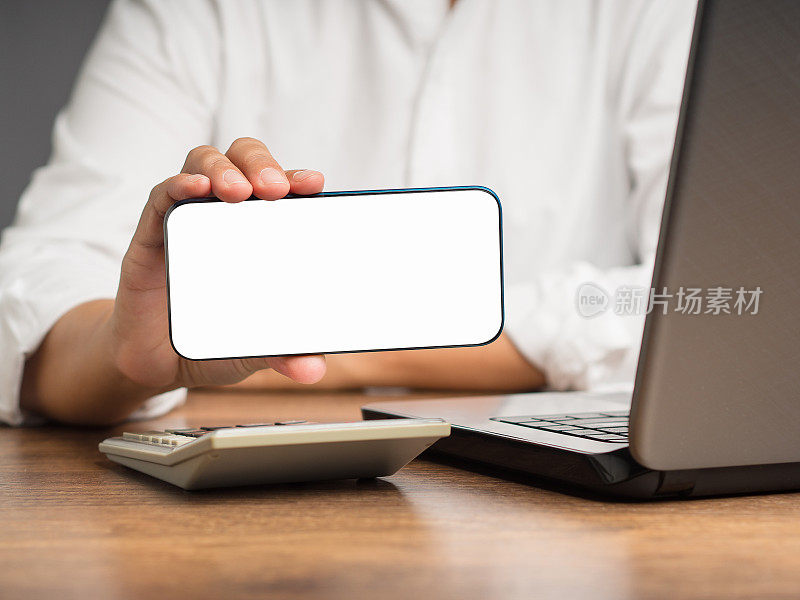 女商人横着拿着一个白色的空白屏幕的智能手机坐在桌子旁