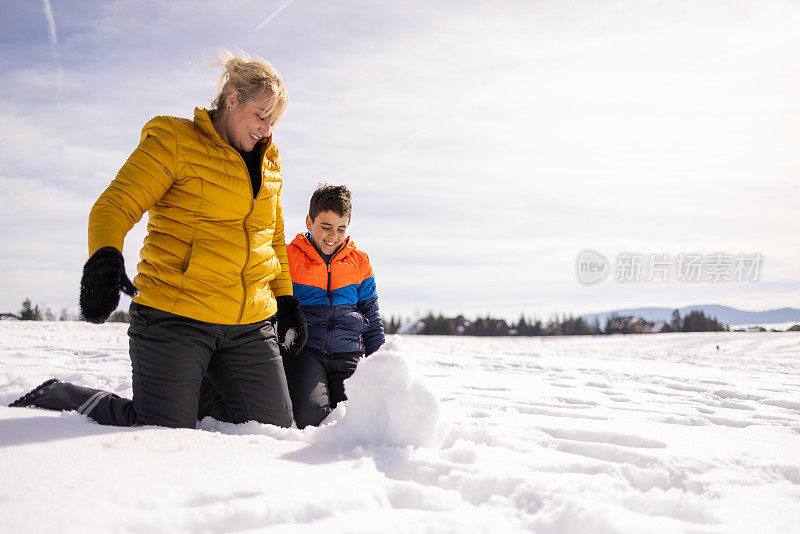 顽皮的高加索儿子和母亲在山上堆雪人