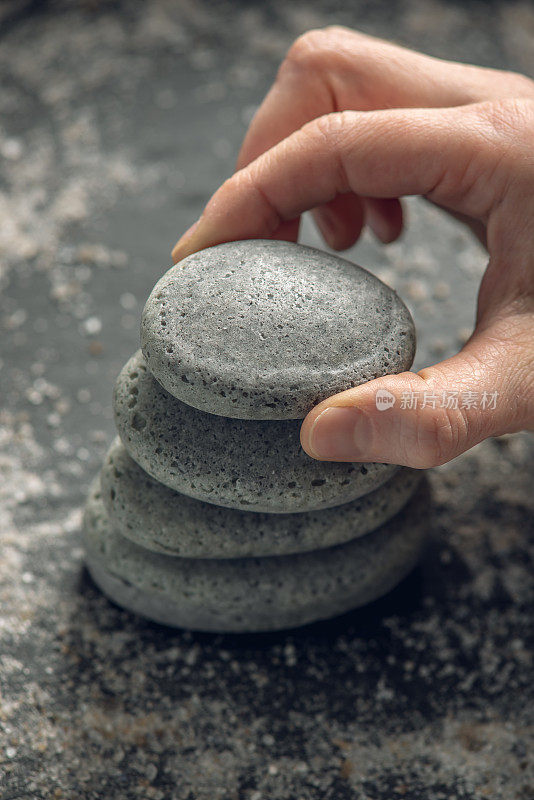 在黑色的背景上，一块块石头堆叠成天然肥皂的形状，上面覆盖着海盐，一只手把石头放在上面。有机化妆品和水疗的概念