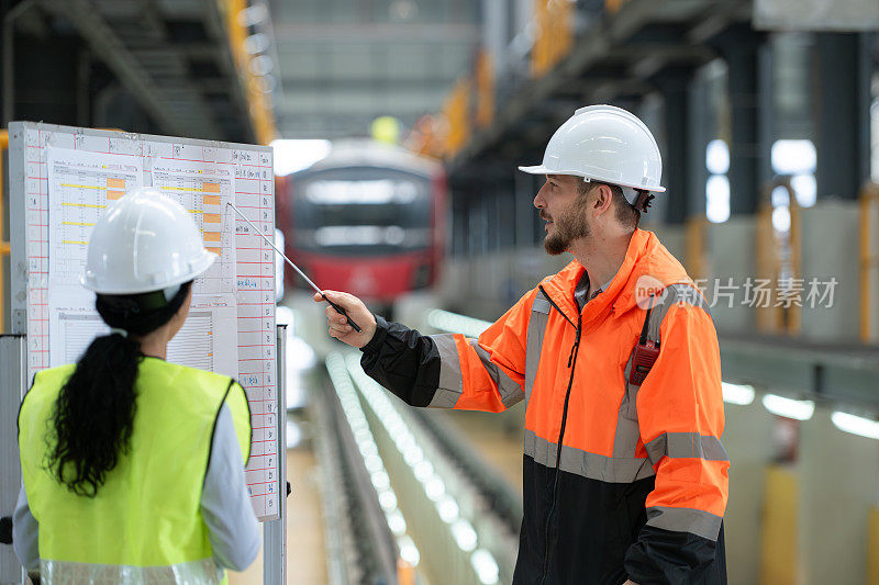 男工程师和女工程师一起在电力维修站工作，查看电力列车维修时间表的详细信息。