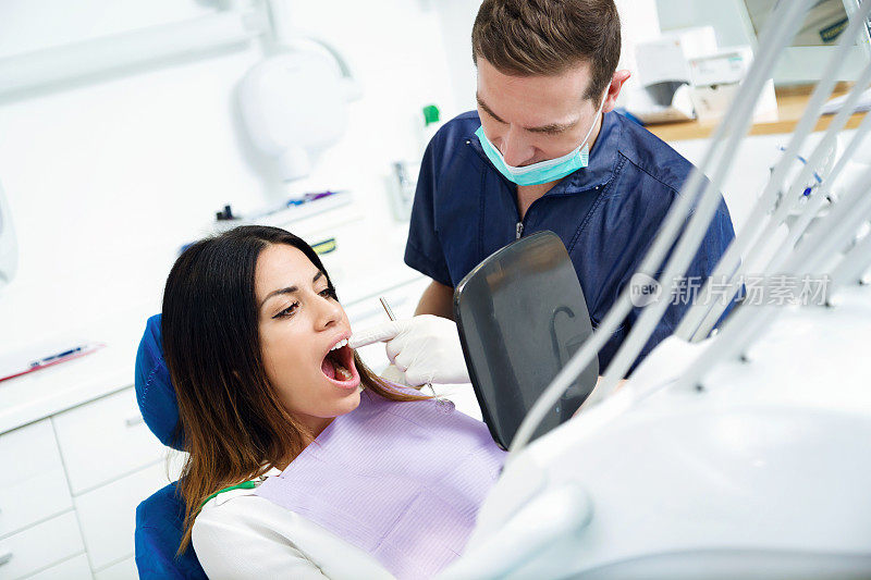 在牙科诊所的镜子前，年轻貌美的牙医和满意的病人看着美白治疗的结果。