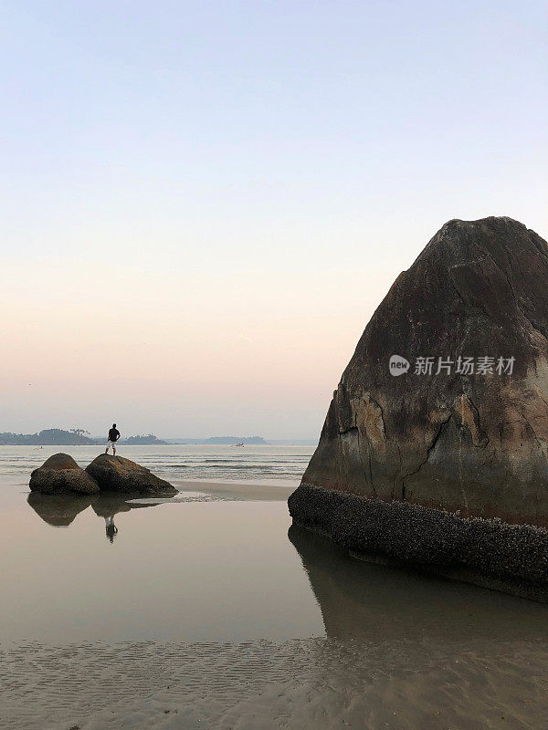 男人看着海边的日落在巨大的海滩岩石反射，果阿海滩，印度，Palolem海滩在退潮，显示海岸线湿沙涟漪