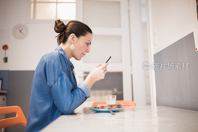 年轻女子在她的厨房里用手机吃早餐