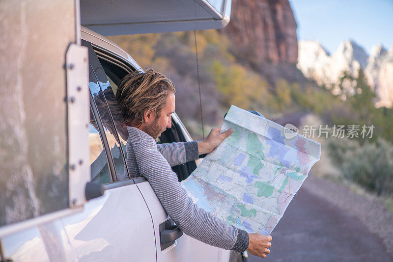 公路旅行概念;一个年轻人在帐篷里看地图寻找方向，探索国家公园和自然，准备冒险。