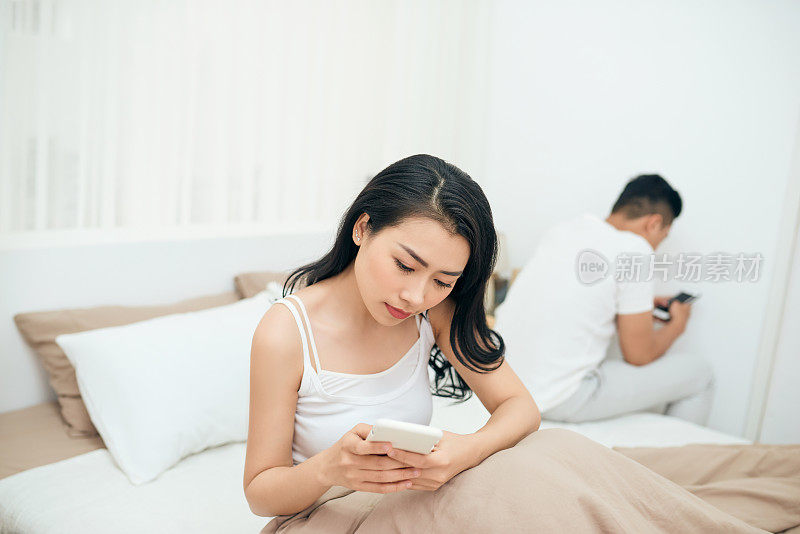 年轻夫妇在床上使用手机，忽视彼此作为陌生人的关系和沟通问题