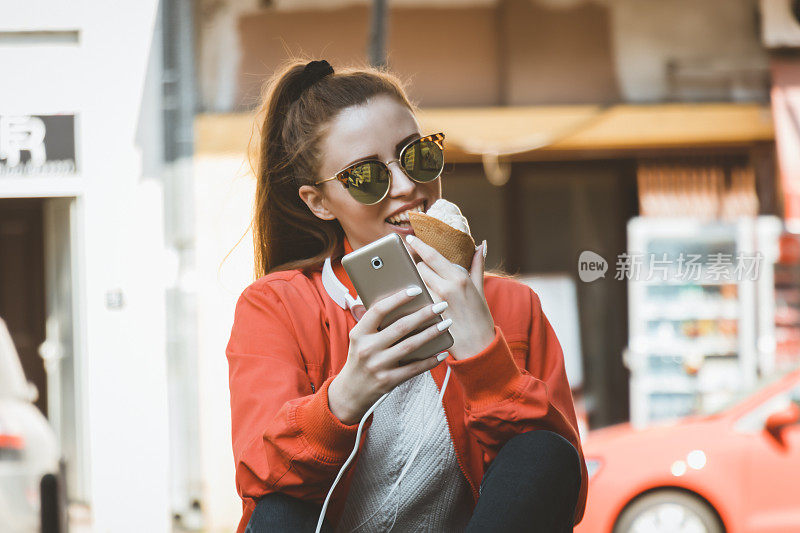 吃着冰淇淋的迷人女人正坐在户外，用智能手机输入信息