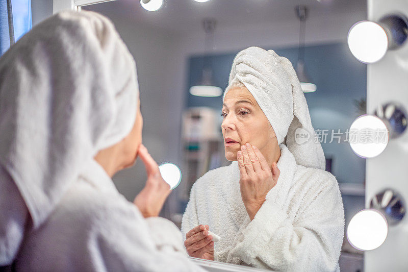 成熟的女人在镜子前收紧脸部皮肤。