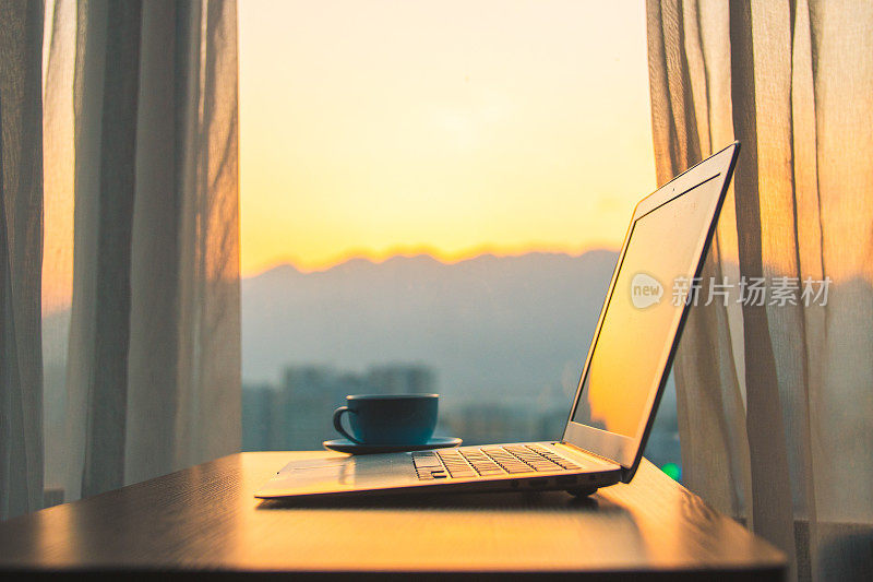 书桌上放着笔记本电脑，窗外是夕阳