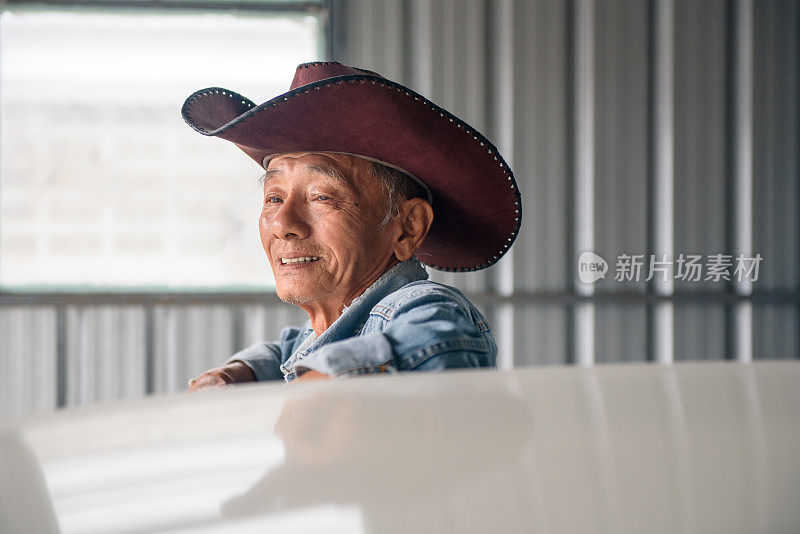 年长的亚洲男人在复古牛仔夹克摆姿势与古董车