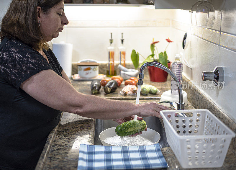 成年妇女在家庭厨房里洗蔬菜，然后把它们放进冰箱