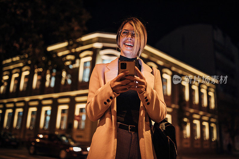 一个快乐的年轻女人在晚上在城市的户外使用手机