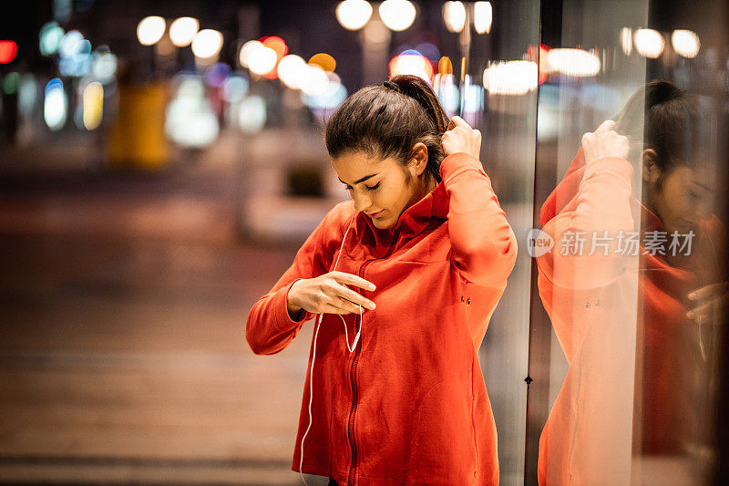 年轻的女运动员在跑步前戴上兜帽和耳机